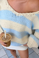 Close-up of the V-neckline and loose chunky knit texture of a light blue and cream striped sweater