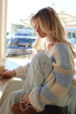 Side view of a light blue and cream striped chunky knit sweater with a V-neck and wide sleeves