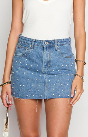 Front view of a mid wash denim mini skirt covered in scattered pearl embellishments with a frayed raw hem