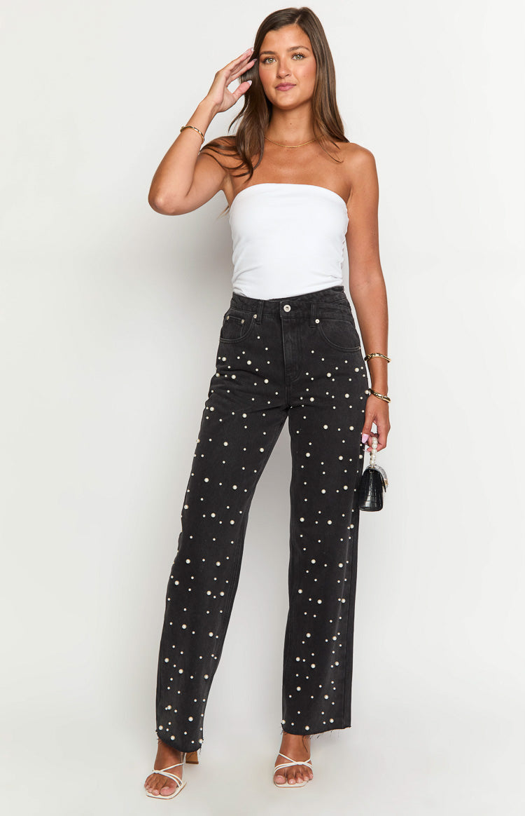 Full length view of black high waisted jeans with all-over pearl embellishments and distressed raw hem
