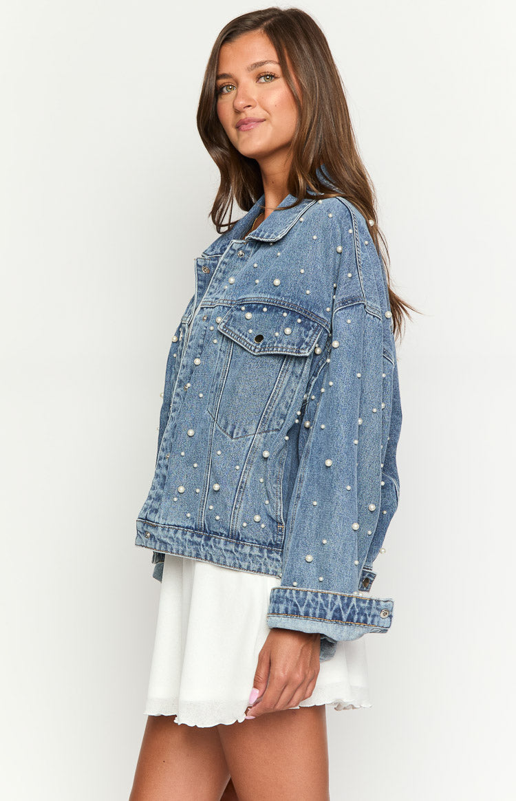 Side view of an oversized mid wash denim jacket with pearl embellishments and cuffed sleeves