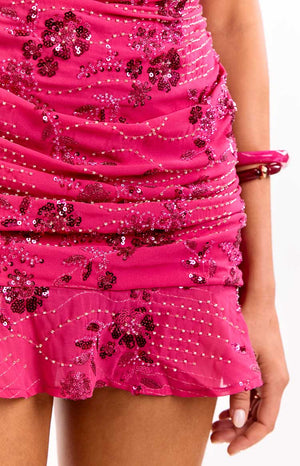 A close-up of our model showing a hot pink strapless mini dress with a ruched bodice. This dress is covered in sequin flowers and beading in shades of dark and light pink.