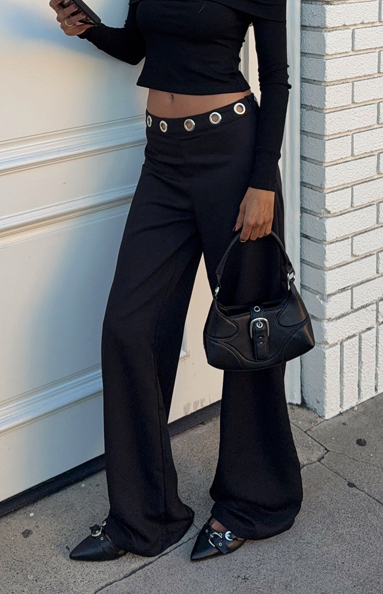 Black straight leg pants with silver eyelets on the waistband, highlighting the relaxed fit and long hem