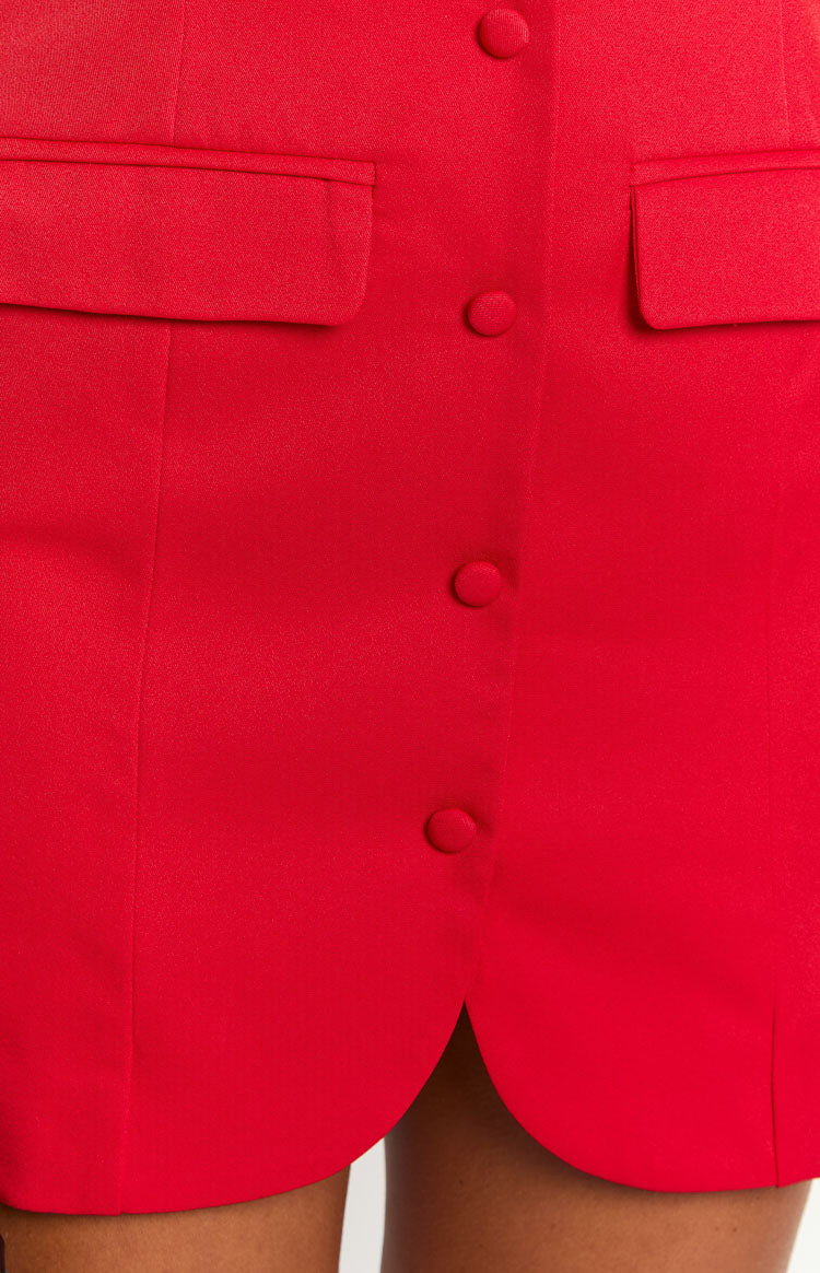 Close-up of the red mini dress showing button-front detail, two flap pockets, and a scalloped hem