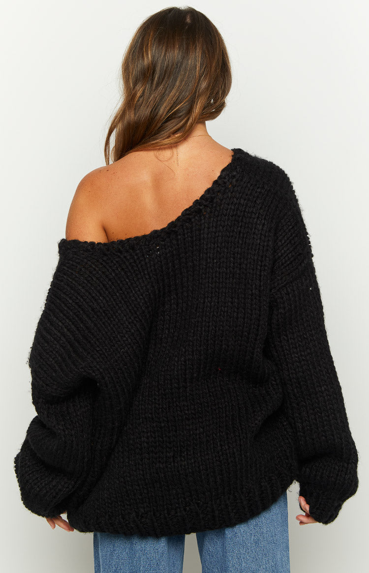 Back view of a black chunky knit sweater with a wide neckline worn off one shoulder