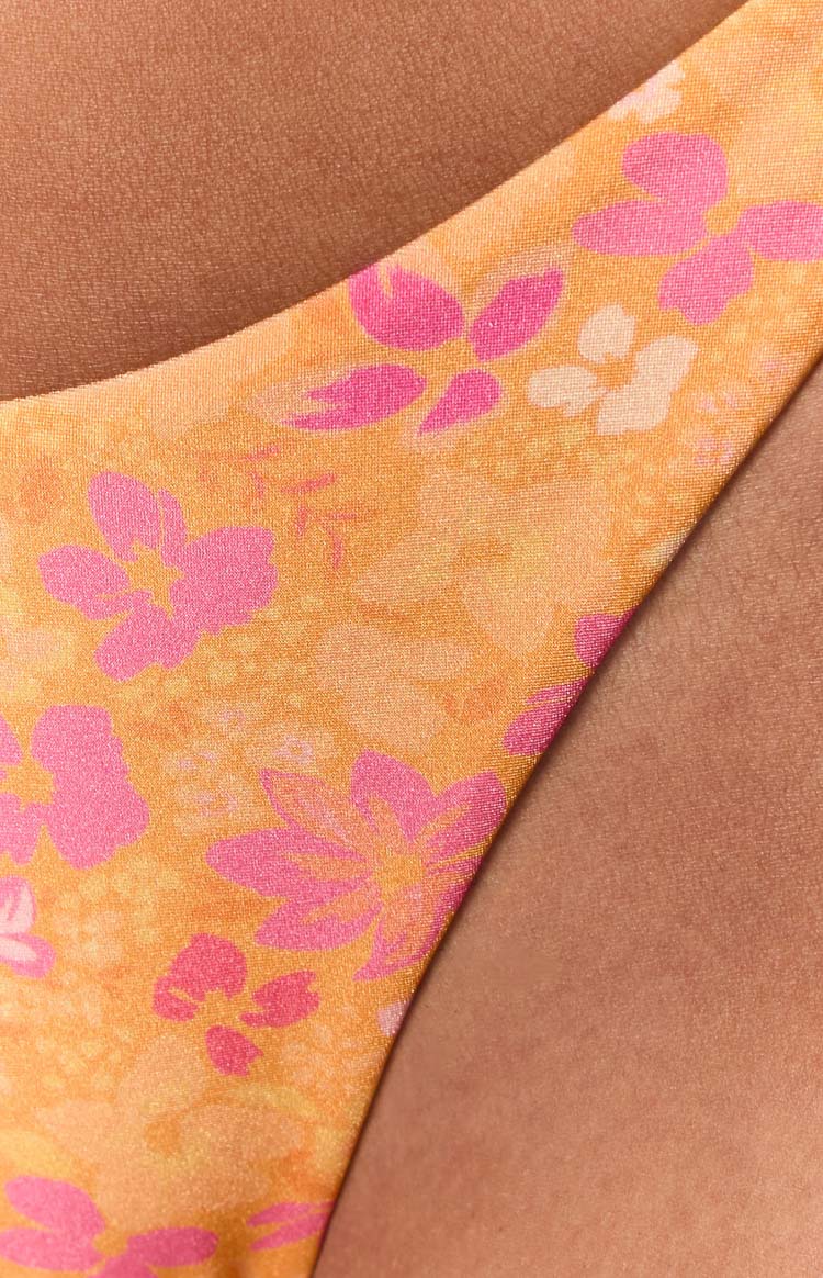 Close-up of the orange bikini bottom fabric with a vibrant pink floral pattern