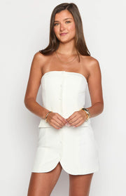 White strapless mini dress with decorative front buttons, a subtle peplum waist, and scalloped hem
