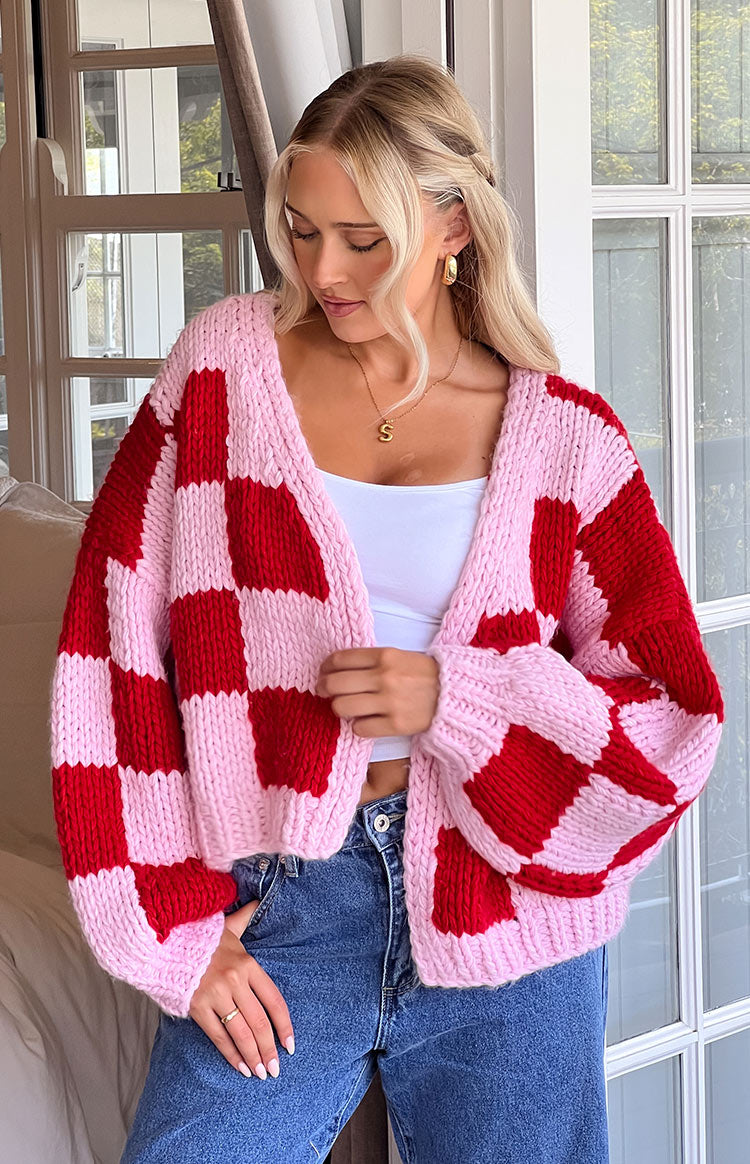 Front view of a pink and red checkerboard chunky knit cardigan with an open front and voluminous sleeves