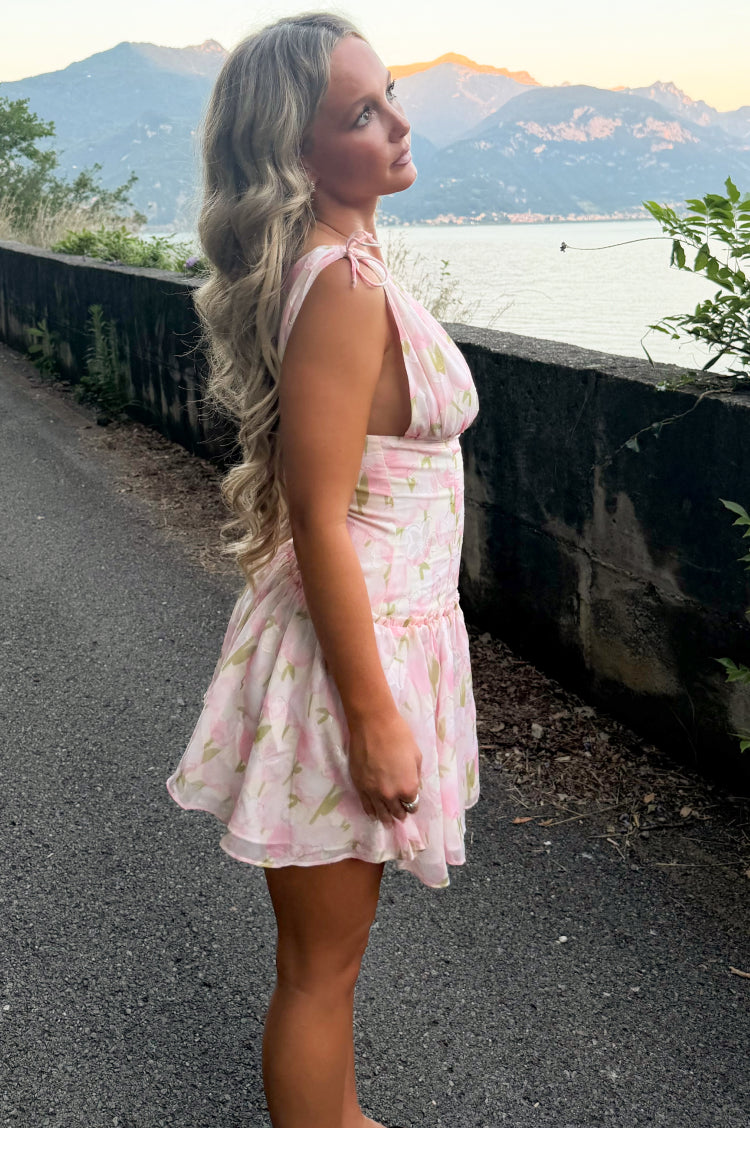 Side view of a pink floral mini dress with tie-shoulder straps, deep armholes, and a ruched waist leading to a flowy tiered s