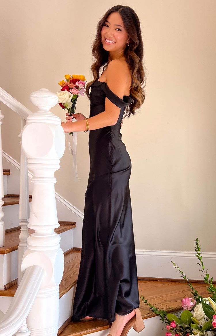 Side view of a black off-shoulder maxi dress with a folded neckline and flowing satin skirt