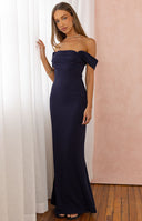 A full-length image of a model wearing a form-fitting navy blue off-the-shoulder maxi dress with a straight neckline.
