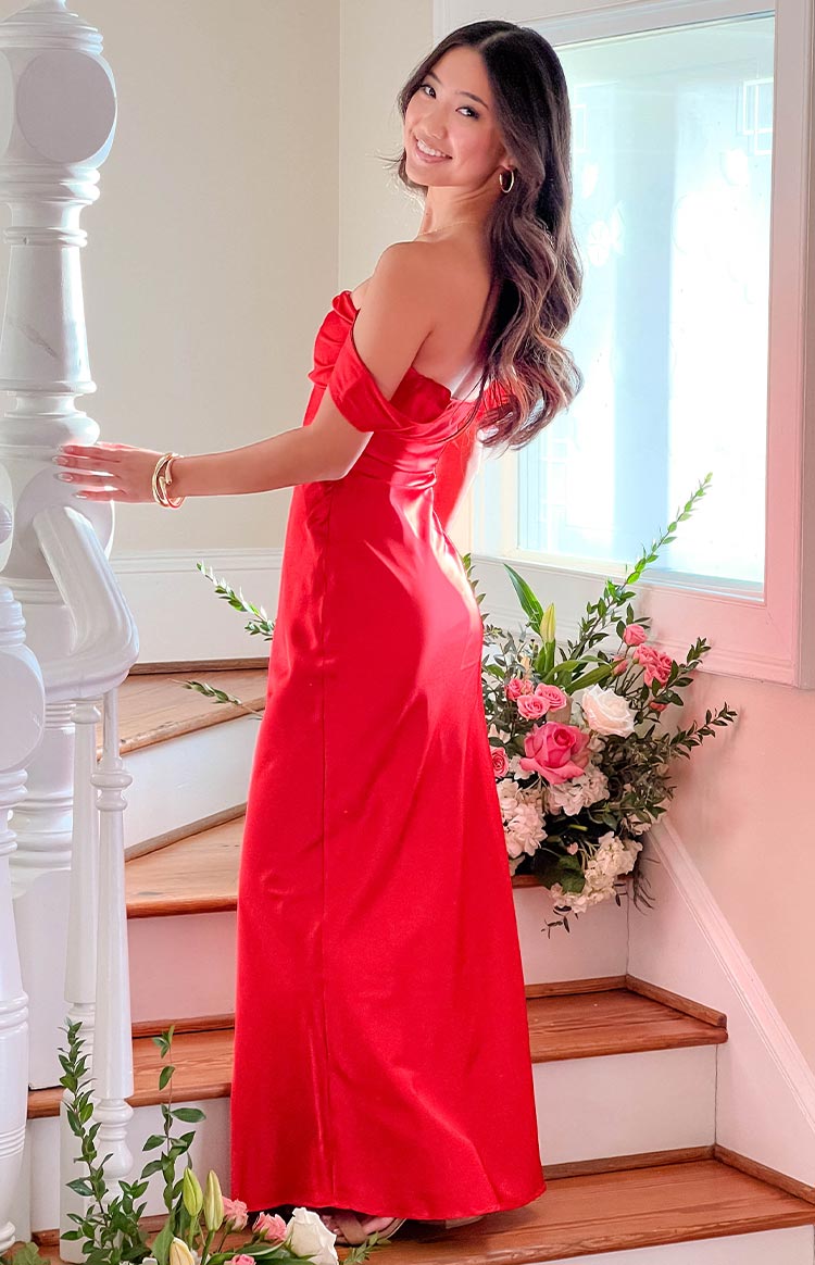 Side view of a red off-shoulder formal dress with a fitted bodice and long flowing maxi skirt