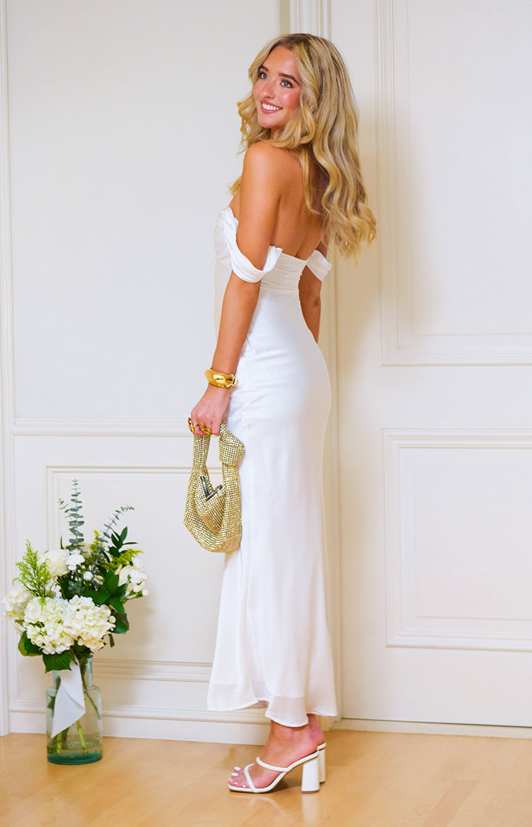 Side view of a white off-shoulder formal dress with gathered sleeves and a flowing maxi skirt