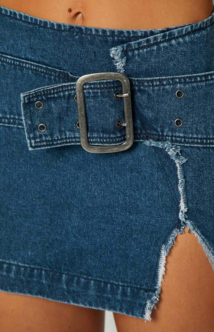 Close-up of the silver buckle, eyelets, and frayed distressed detailing on the blue denim mini skirt