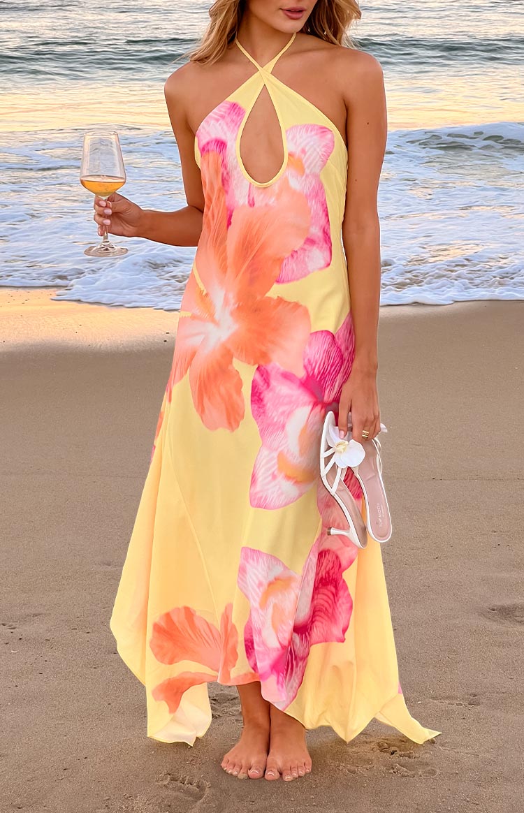 Full length view of a flowy yellow maxi dress with large pink and orange hibiscus floral print and a halter keyhole neckline