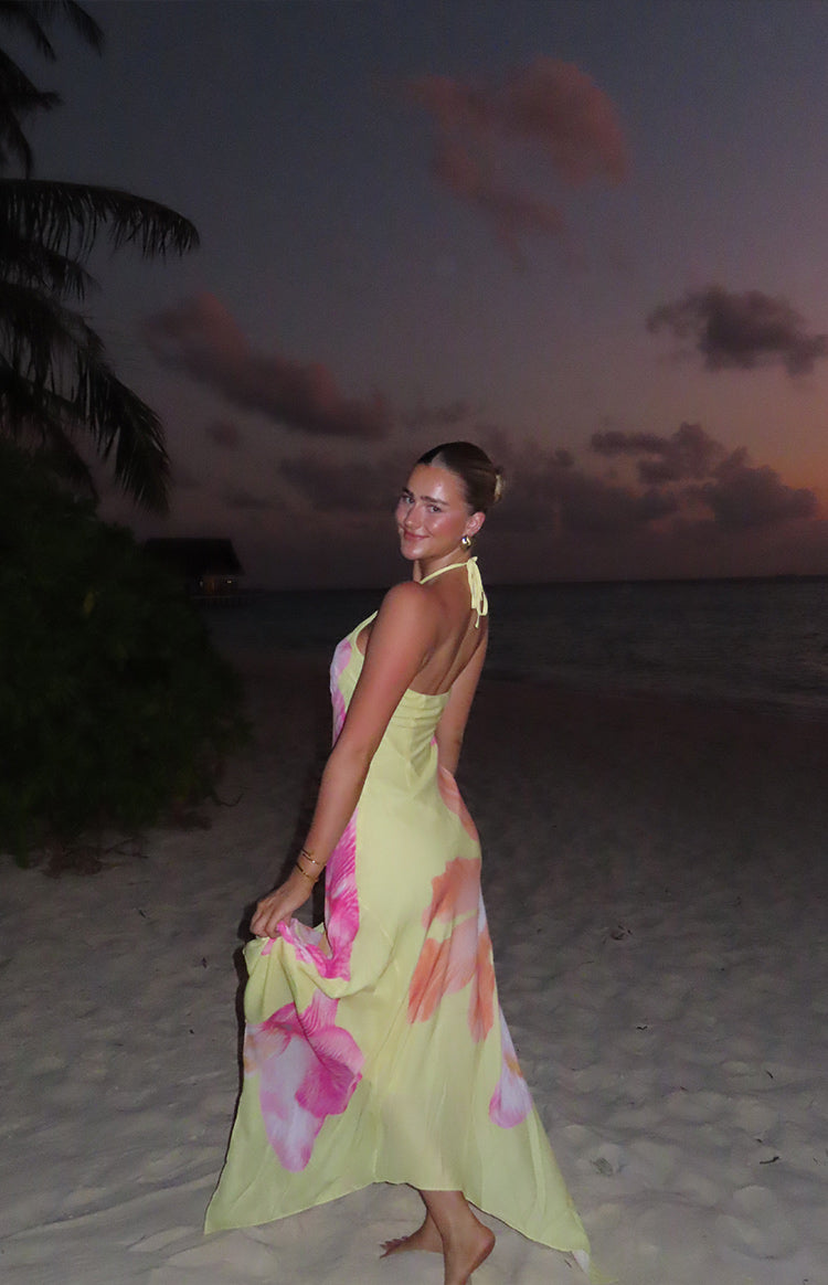 Back view of a yellow hibiscus floral maxi dress with a tie halter neck and a full, flowing skirt