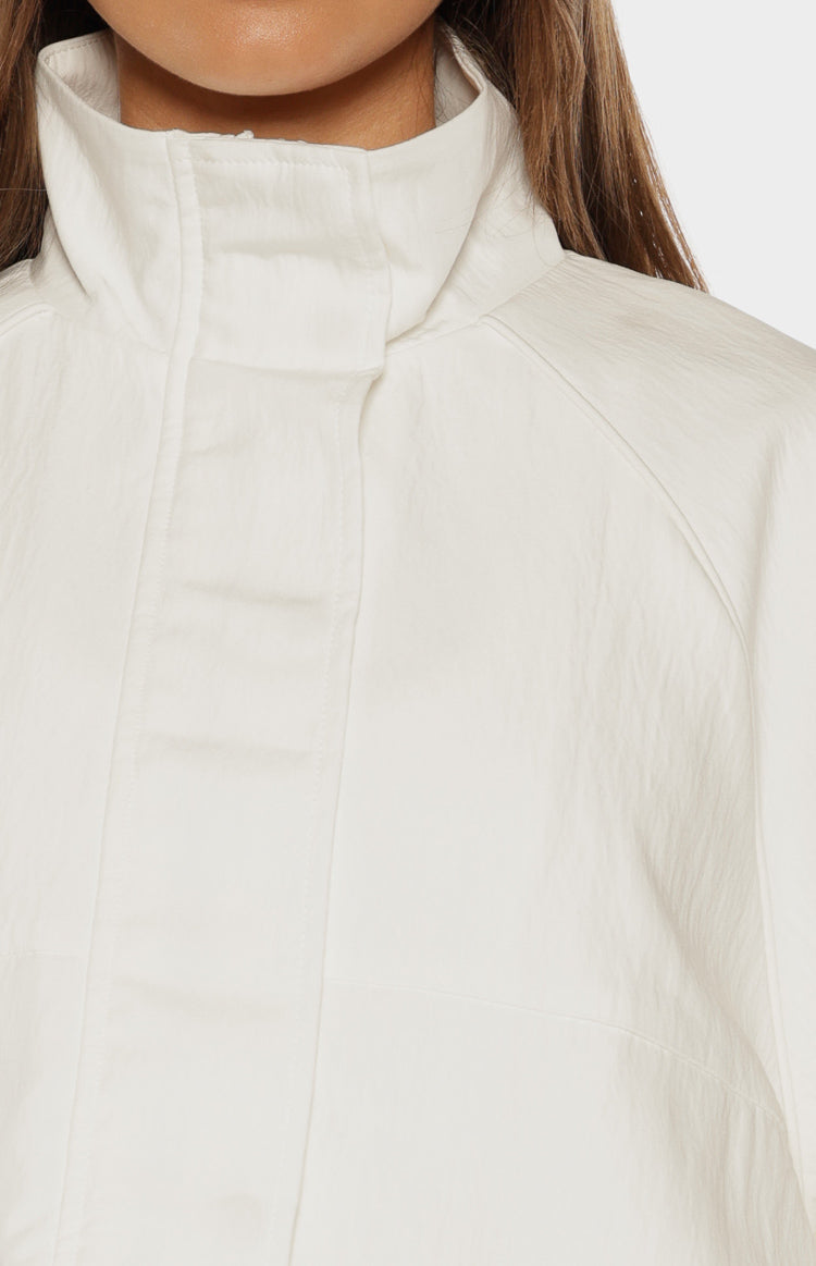 Close-up of the cream funnel neck sports jacket showing the crinkled fabric texture and raglan sleeve seam
