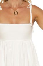 Close-up of the white mini dress showing tie-up shoulder straps, side zipper, and gathered waist