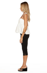 Side view of a white denim top with tie-shoulder straps and a flared peplum hem
