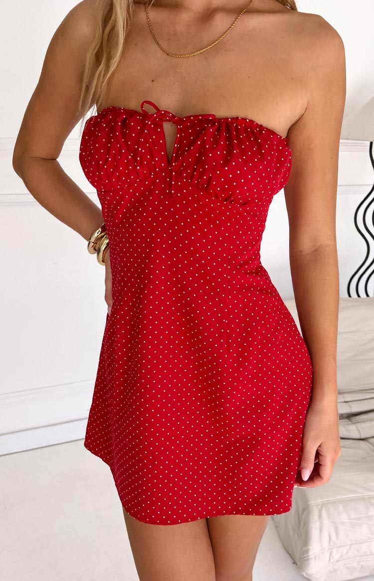 Angled view of the red polka dot mini dress with a ruched strapless neckline and tie-front keyhole