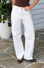 Full length view of white wide-leg denim jeans with brown contrast stitching and frayed raw hem
