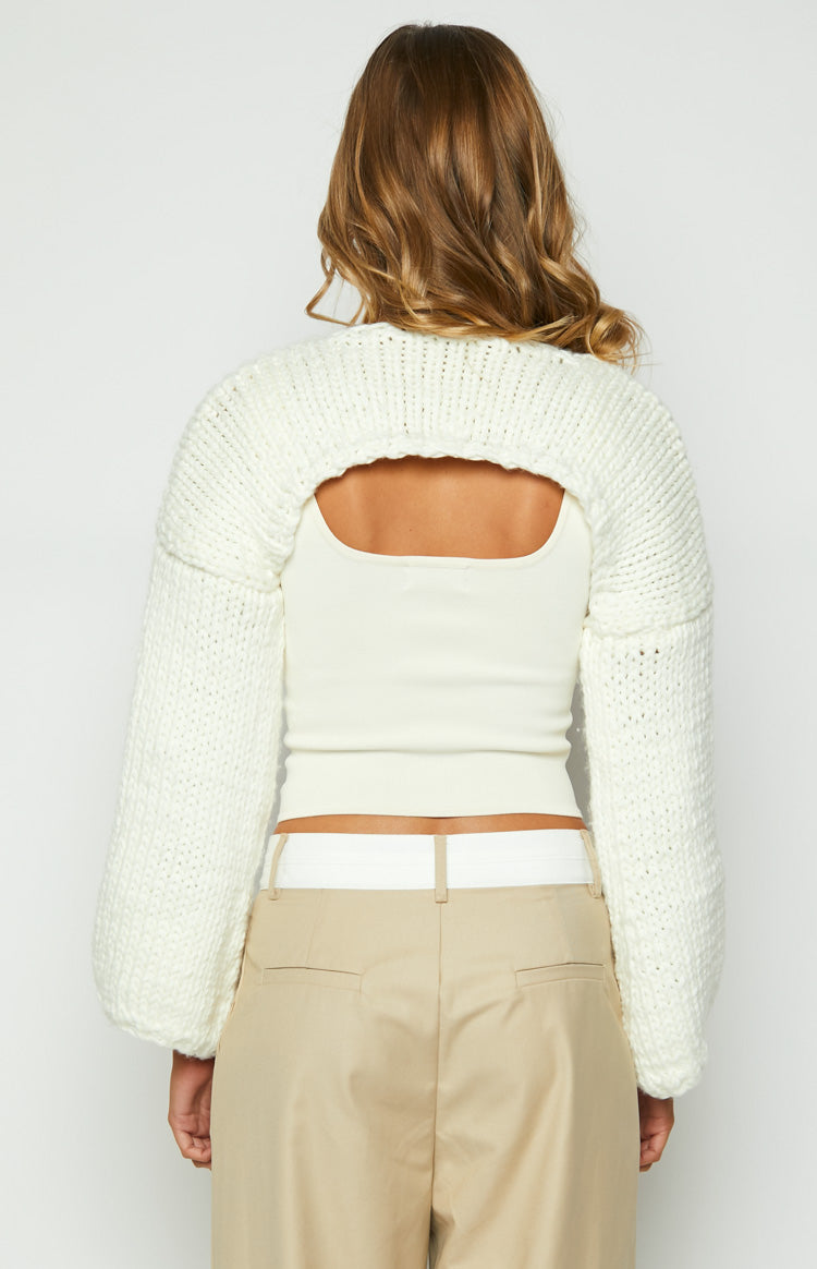 Back view of the cream chunky knit shrug featuring an open back and long, full sleeves