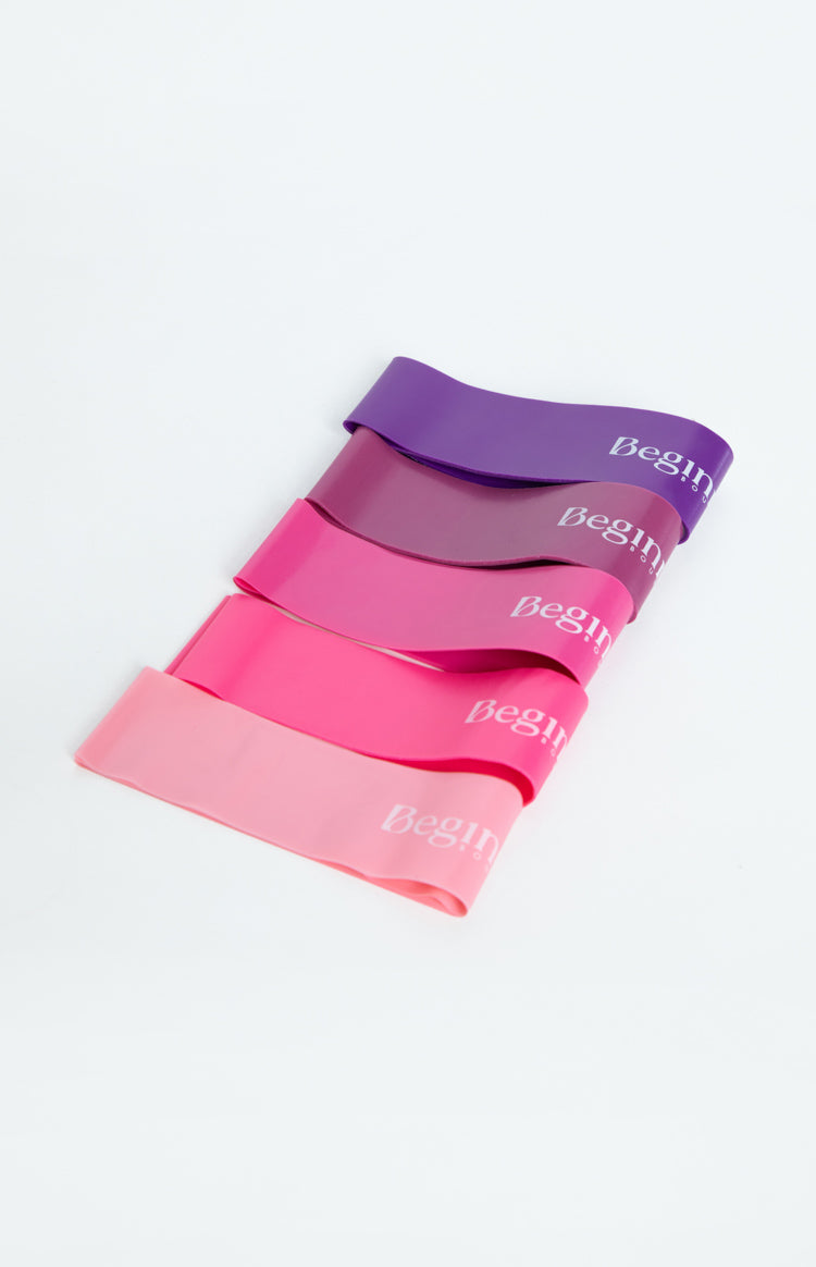 Five resistance bands fanned out in a gradient from dark purple to light pink, each with 'Begin' logo