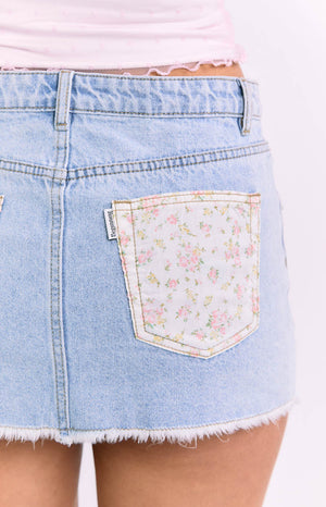 Close-up of the light wash denim skirt's back pocket, featuring a white floral print with pink and yellow flowers, and frayed hem