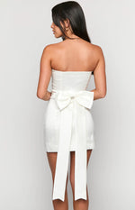 Rear view of a white strapless mini dress featuring a large satin bow at the back waist with long tails
