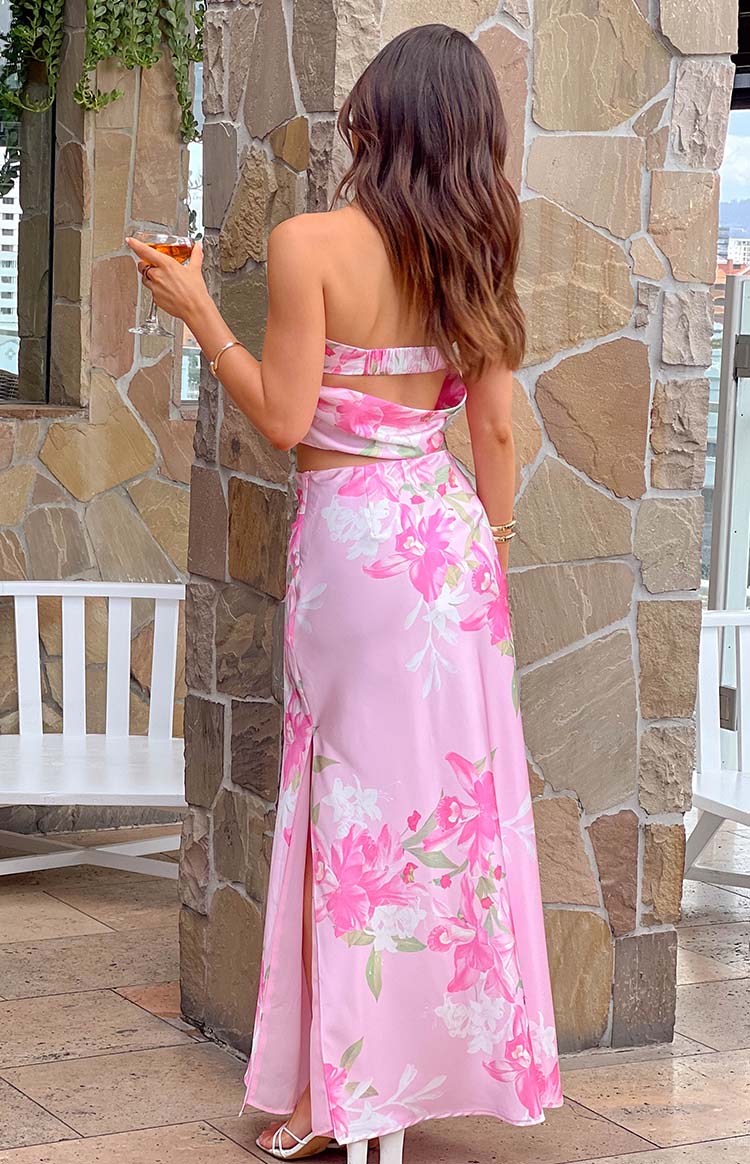 Rear view of a flowy pink floral print maxi skirt with large pink and white flowers, green leaves, and a high side slit on the left leg