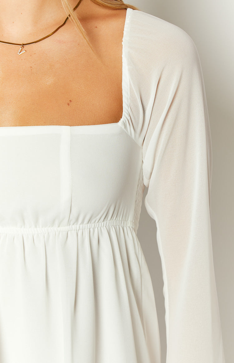 Close-up of the white chiffon mini dress showing the square neckline, sheer long sleeve, and shirred elastic waist