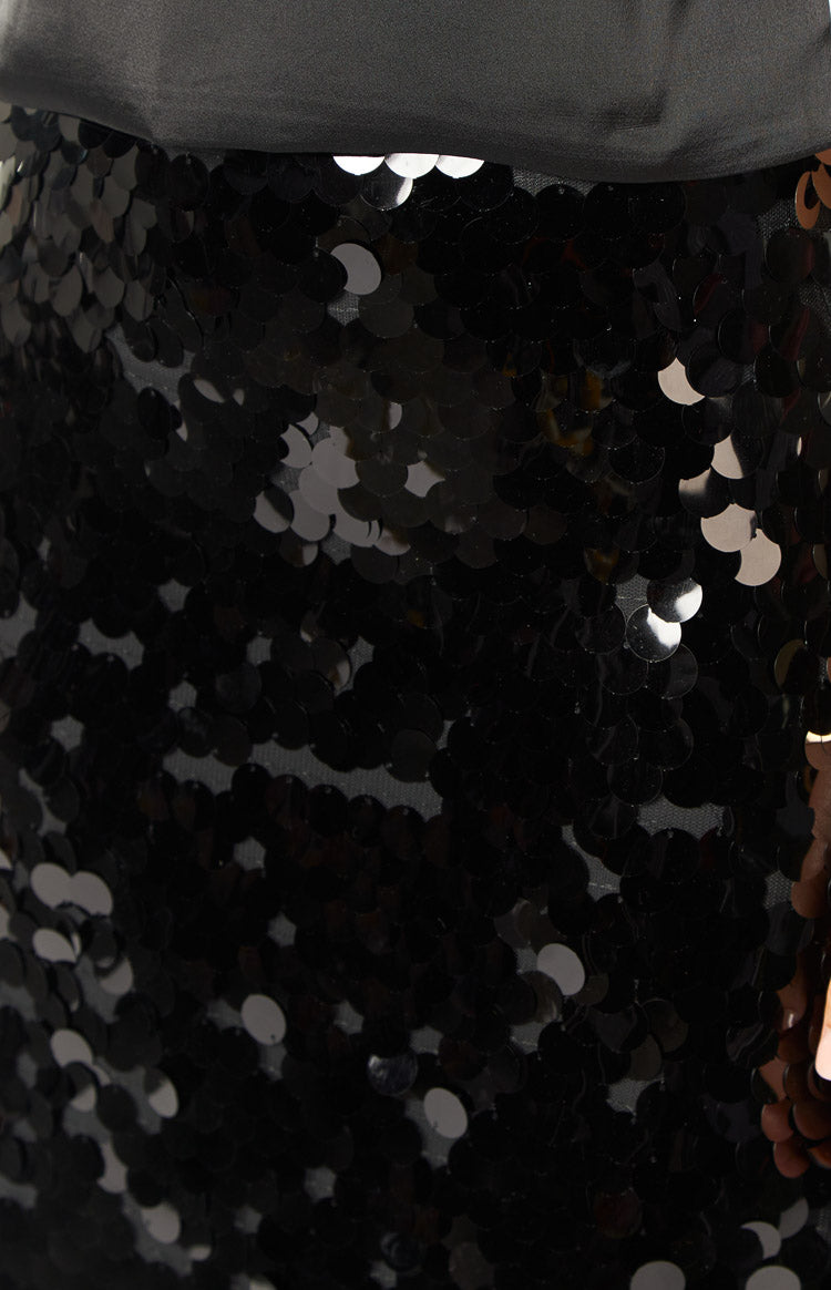 Close-up of black overlapping round sequins on a maxi skirt, with a smooth black fabric waistband and glimpses of the black mesh base