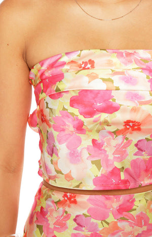 A close-up of a strapless crop top in a pink coral and yellow floral print on a satin-like fabric showing a gathered or folded detail across the bust.