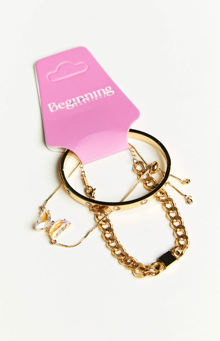 Close-up of a gold bangle with clear stones, a delicate chain with an iridescent butterfly, and a thick gold curb chain bracelet