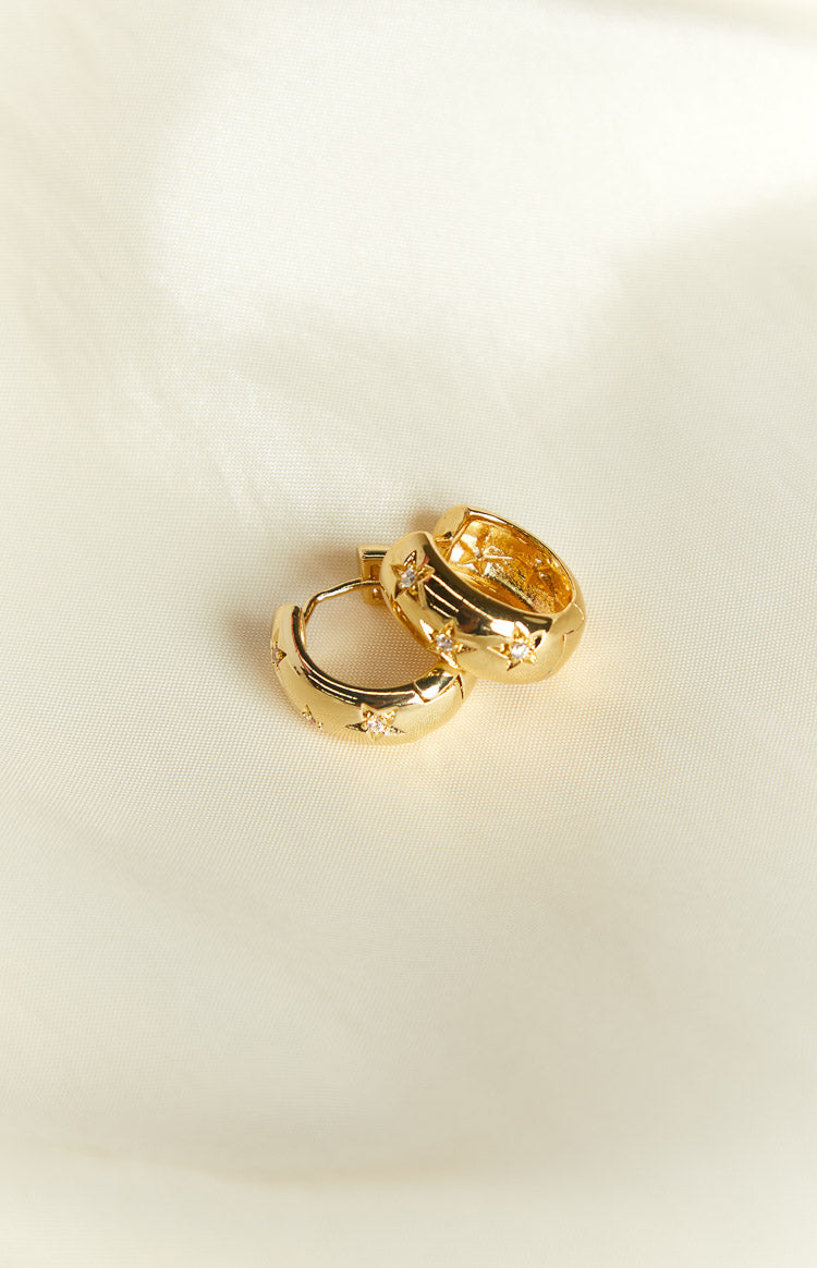 Close-up of two gold chunky hoop earrings with star cutouts and clear crystal embellishments