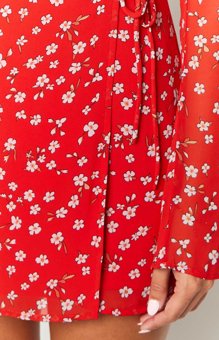 Close-up of the red floral print fabric, highlighting the wrap front detail with ties and long sleeve