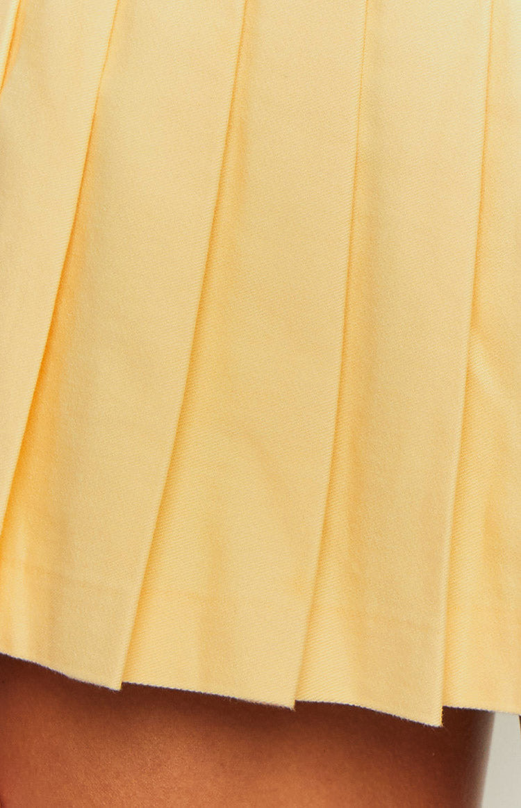 Close-up of the neatly folded pleats and woven fabric of the yellow mini dress skirt