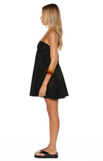 Side view of a black mini dress with thin spaghetti straps and a gathered bust with eyelet embroidery, showing the flowy A-line skirt