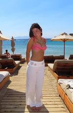 Front view of white wide-leg pants with floral cutout detail on the waistband, beach