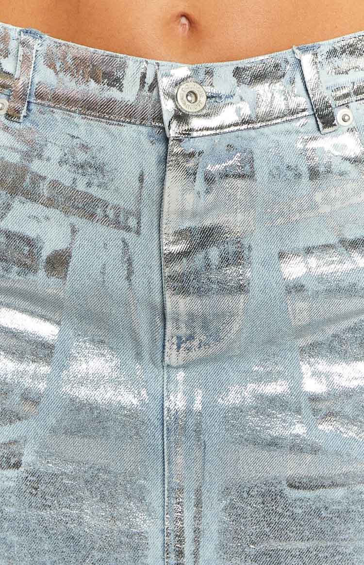 Close-up of the metallic silver pattern on the light blue denim mini skirt's button fly and waistband