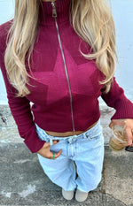 Burgundy knit sweater with a subtle knit star pattern, full zip front, high mock neck, and ribbed cuffs