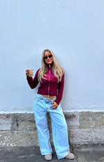 Cropped burgundy knit sweater with a prominent star pattern on the front and high zip neck