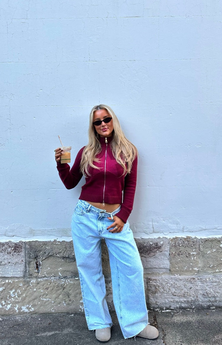 Cropped burgundy knit sweater with a prominent star pattern on the front and high zip neck
