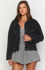 Front view of a black washed oversized denim jacket with a collared neckline, button-front, and distressed hem