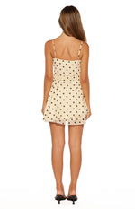 Rear view of a cream polka dot mini dress with a square back, thin straps, and tiered ruffle skirt