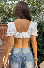 Rear view of a white crop top with square back neckline, puffed broderie trim sleeves, and shirred hem