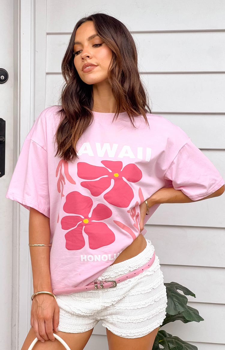 Close-up of a pink oversized tee featuring a large HAWAII HONOLULU graphic and two pink hibiscus flowers