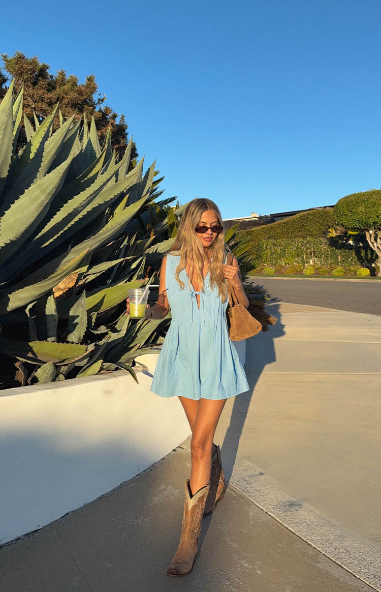 Front view of a light blue playsuit with a tie-front V-neck, sleeveless design, and pleated shorts