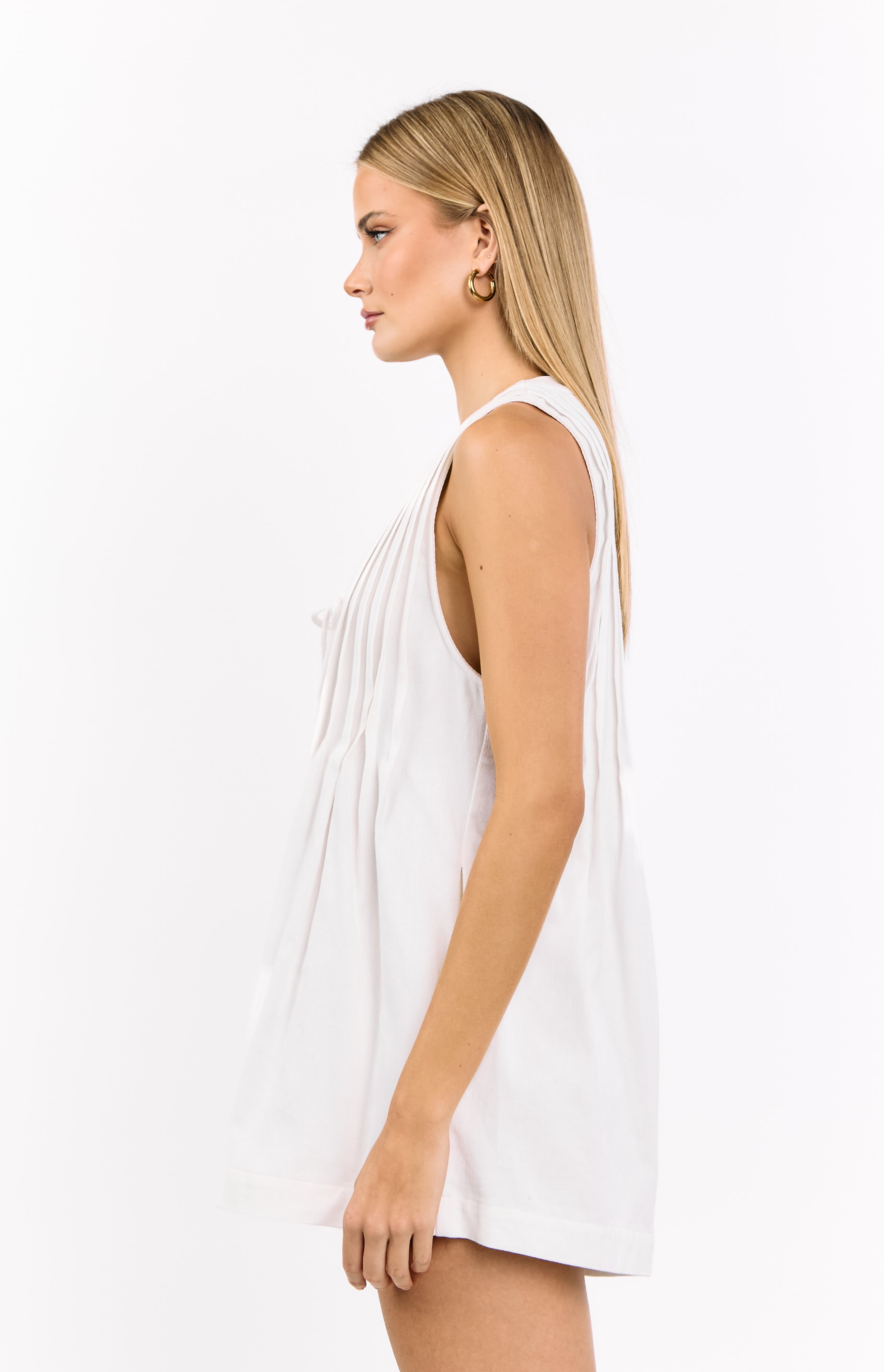 Side view of a white sleeveless playsuit with a relaxed fit and pleated bodice