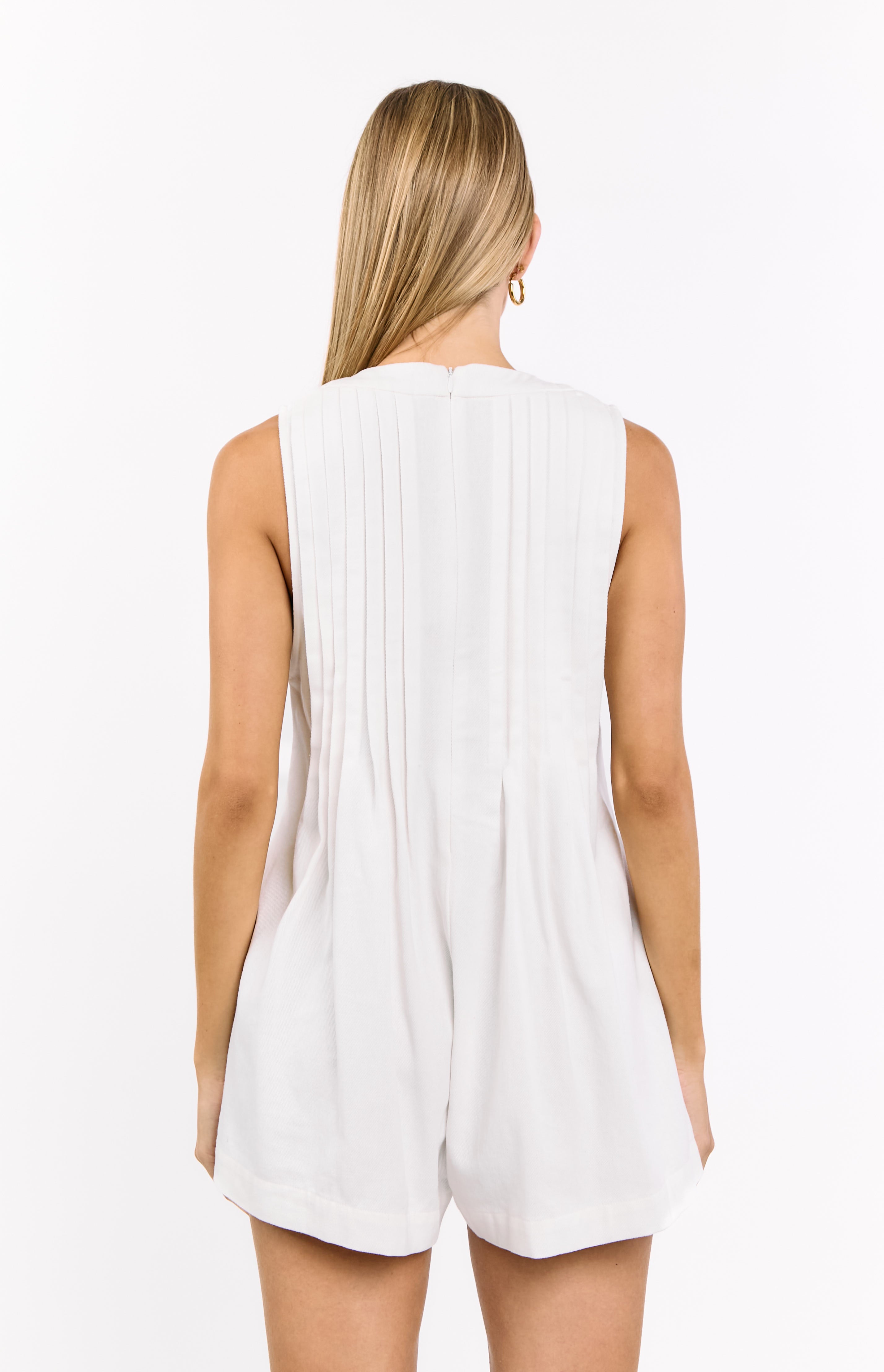 Rear view of a white sleeveless playsuit with vertical pleats on the back bodice and a zipper closure